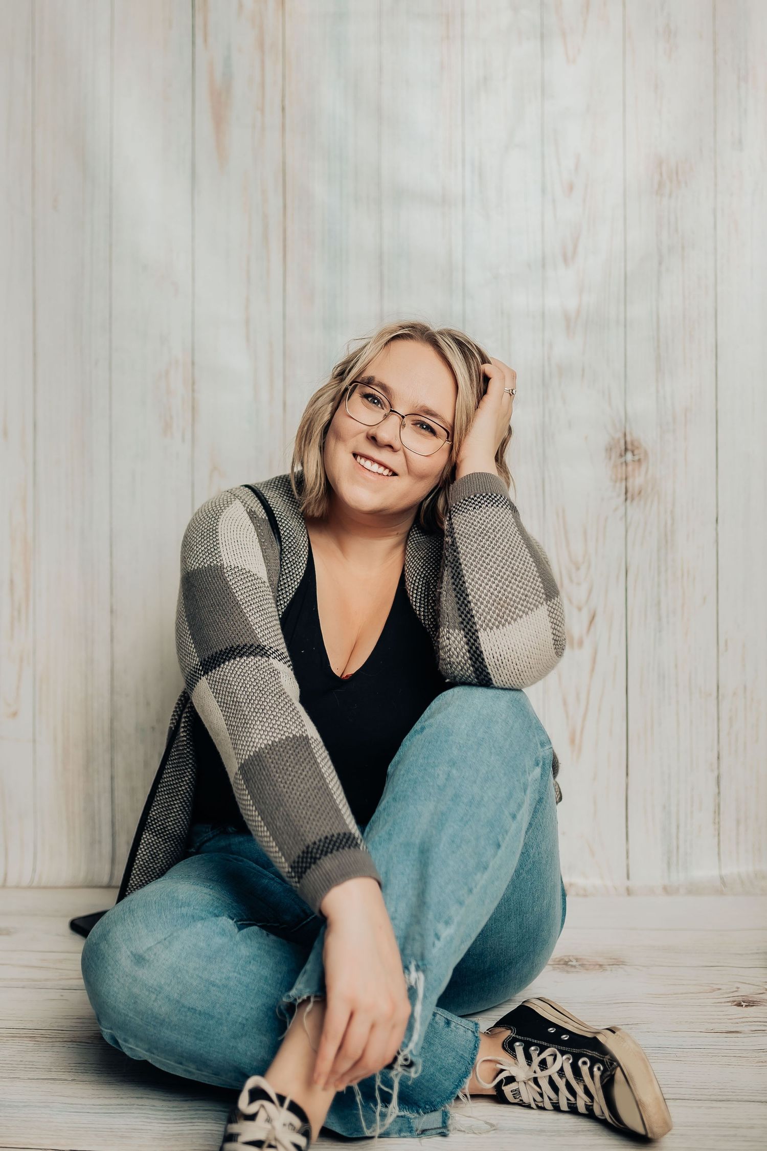 Casual lifestyle portrait against white wooden wall wearing plaid cardigan and glasses.