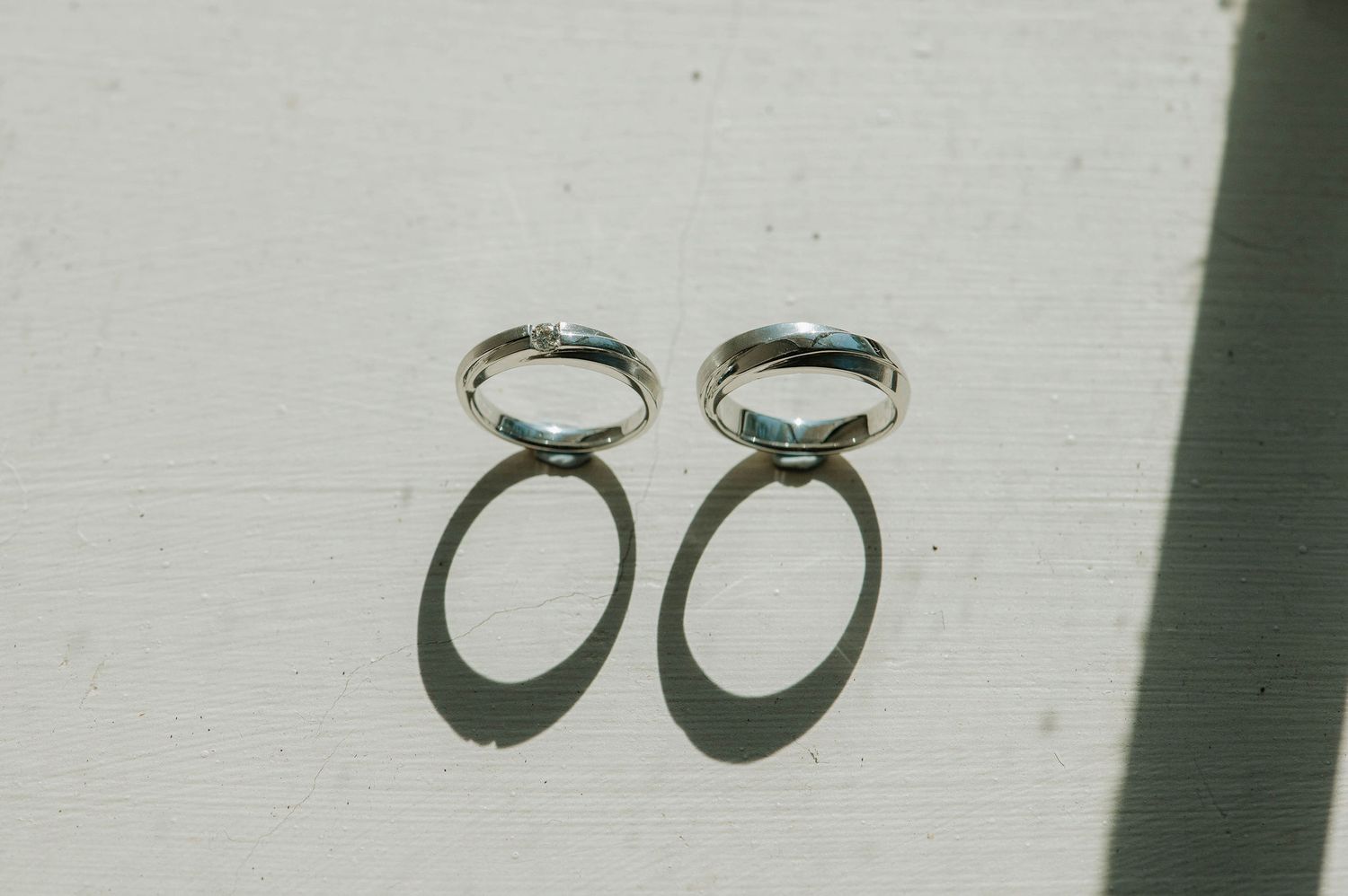 Two wedding rings casting shadows on white surface in artistic composition.