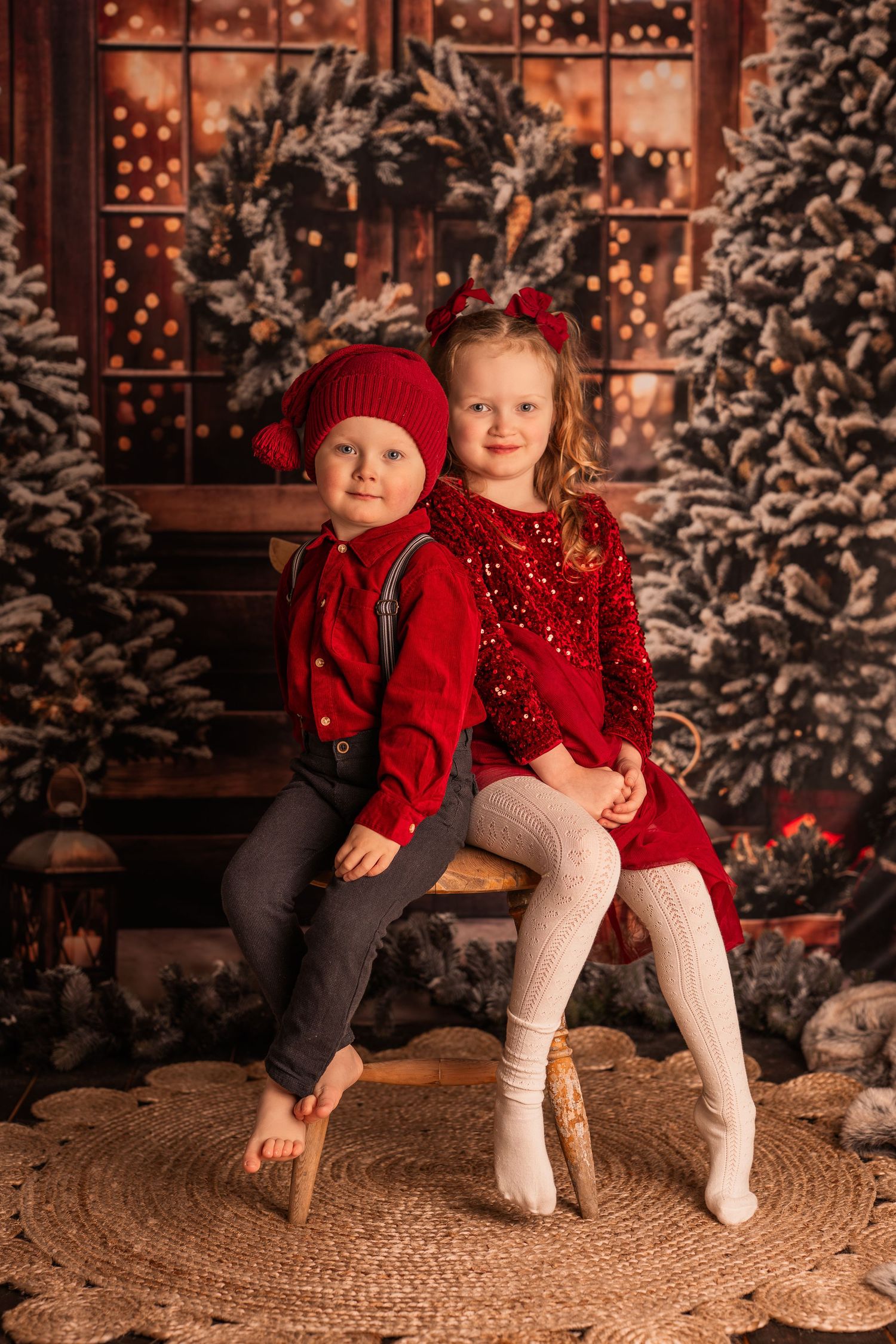 A baby in red clothing sits excitedly on a chair surrounded by Christmas decorations and presents.