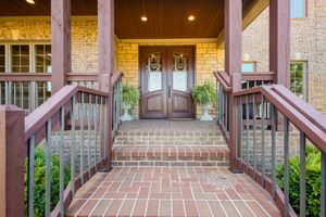Front entrance of luxury home with brick steps, wood railings, and double doors framed by decorative stonework.