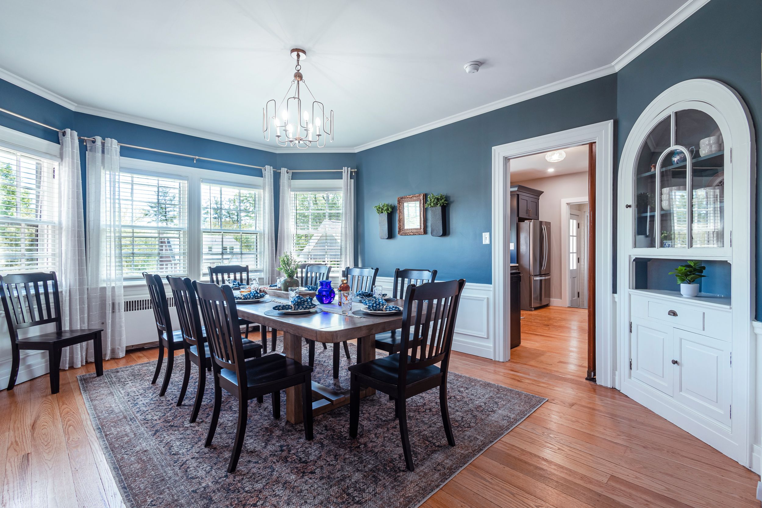 Spacious dining room with blue walls, white trim and elegant chandelier in open floor plan setting.