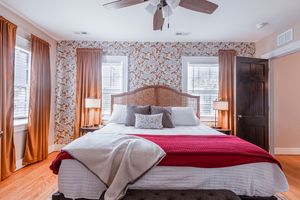 Guest bedroom featuring floral wallpaper, red bedding accents and hardwood flooring.