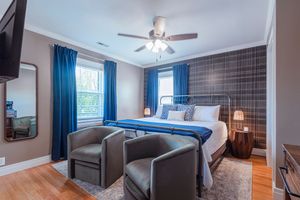 Modern bedroom with plaid accent wall, bright blue curtains, hardwood floors and two gray armchairs.