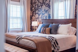 Contemporary bedroom with floral wallpaper, wooden headboard, and layered bedding.