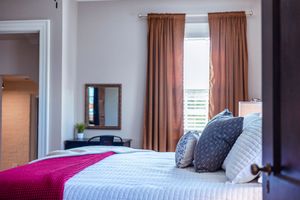 Modern bedroom with mauve curtains, white bedding, and natural light from windows.