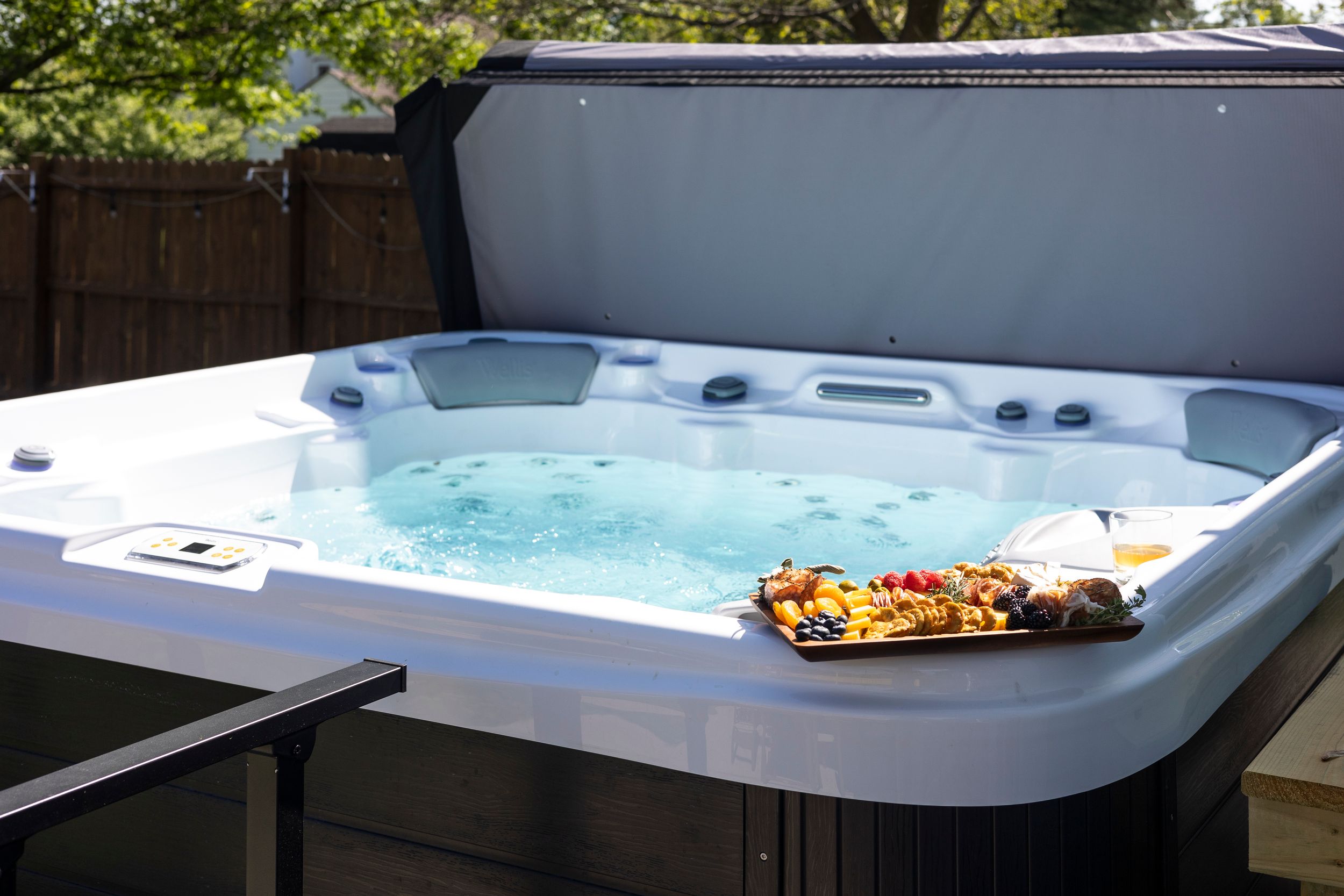 Aerial view of hot tub and patio furniture on wooden deck with green lawn and trees in background.