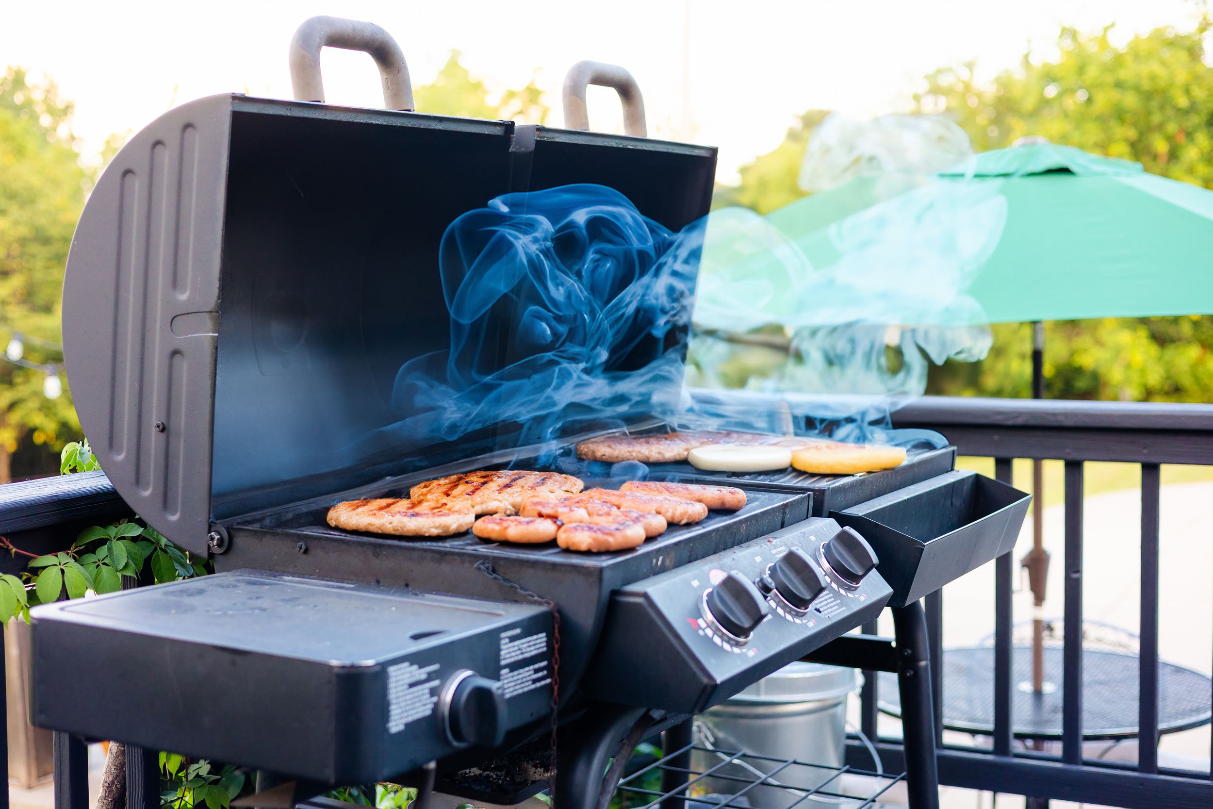 A row of outdoor grills on a deck with smoke rising from cooking food at sunset.