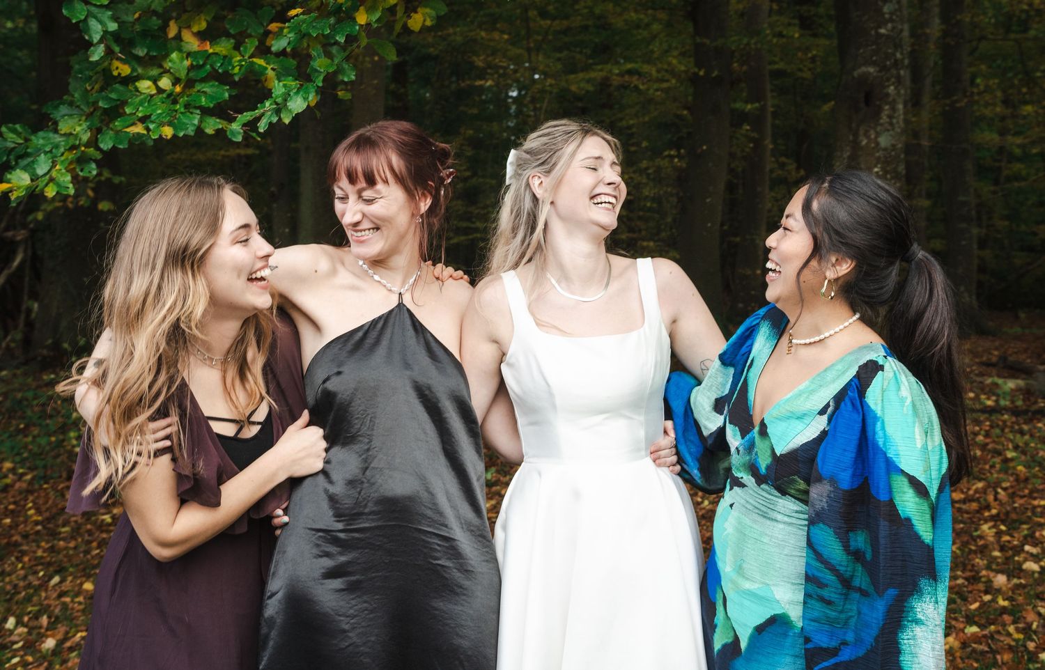 A group of people wearing colorful dresses and outfits gather together in a wooded outdoor setting.