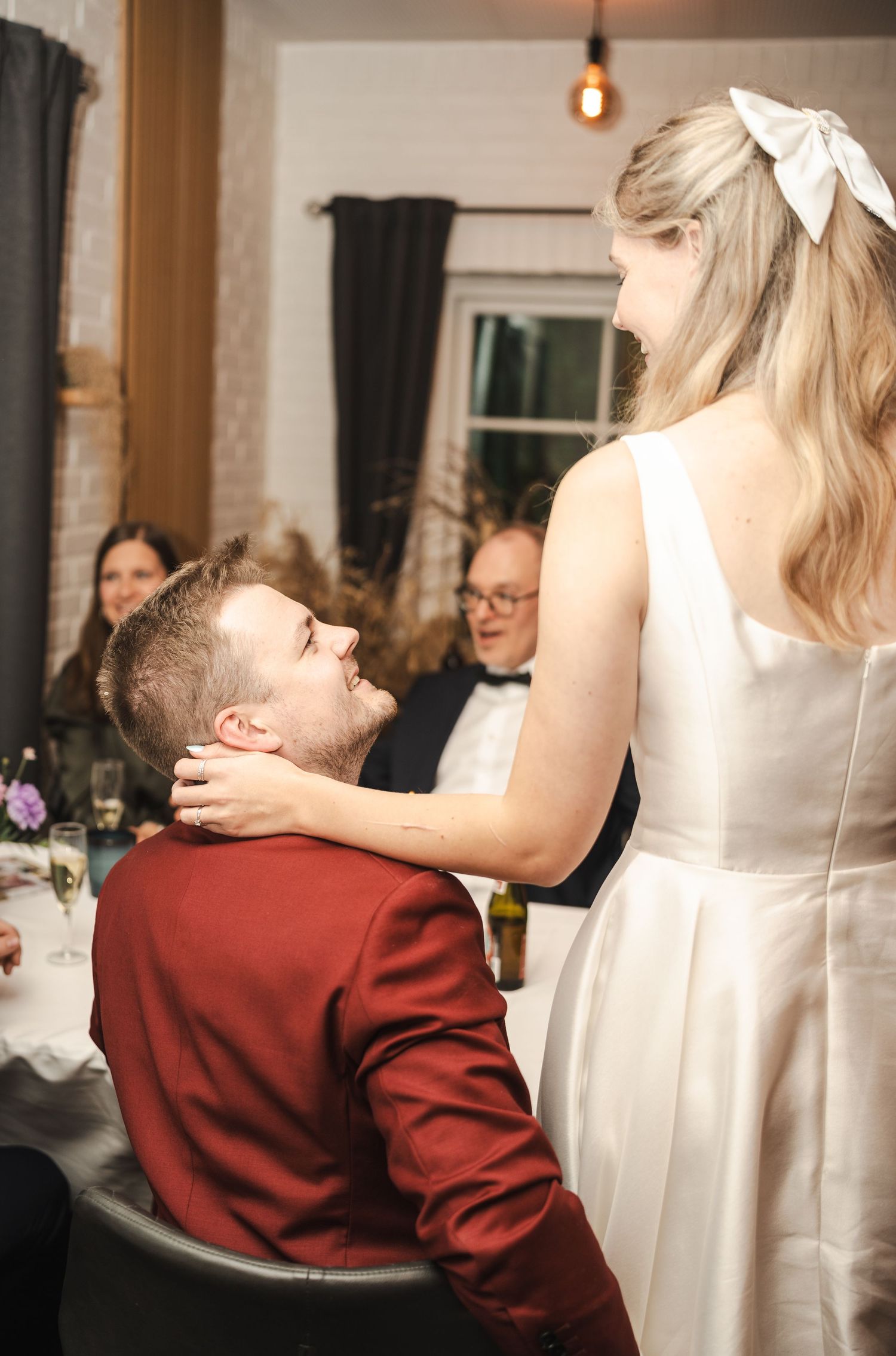 A tender moment at a wedding reception shows a couple sharing an intimate gesture in a decorated indoor venue.
