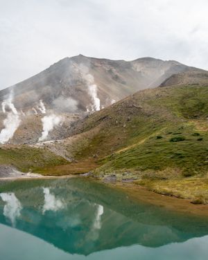 Turquoise alpine lake reflecting steaming volcanic mountains in a dramatic landscape.