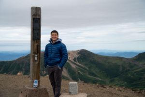 Summit marker post stands against dramatic mountain landscape backdrop.