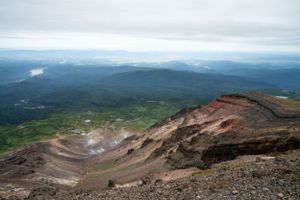Sweeping mountain vista showing volcanic crater and distant valleys under cloudy skies.