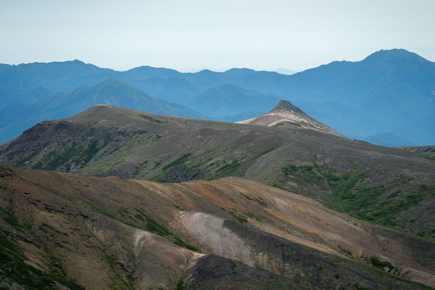 Panoramic view of jagged mountain peaks against a blue sky in a remote wilderness landscape.