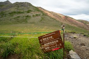 Wooden trail markers stand along a grassy mountain path with scenic valley views.