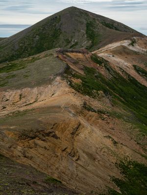 Steep mountainside reveals exposed rock formations and winding trails through alpine vegetation.