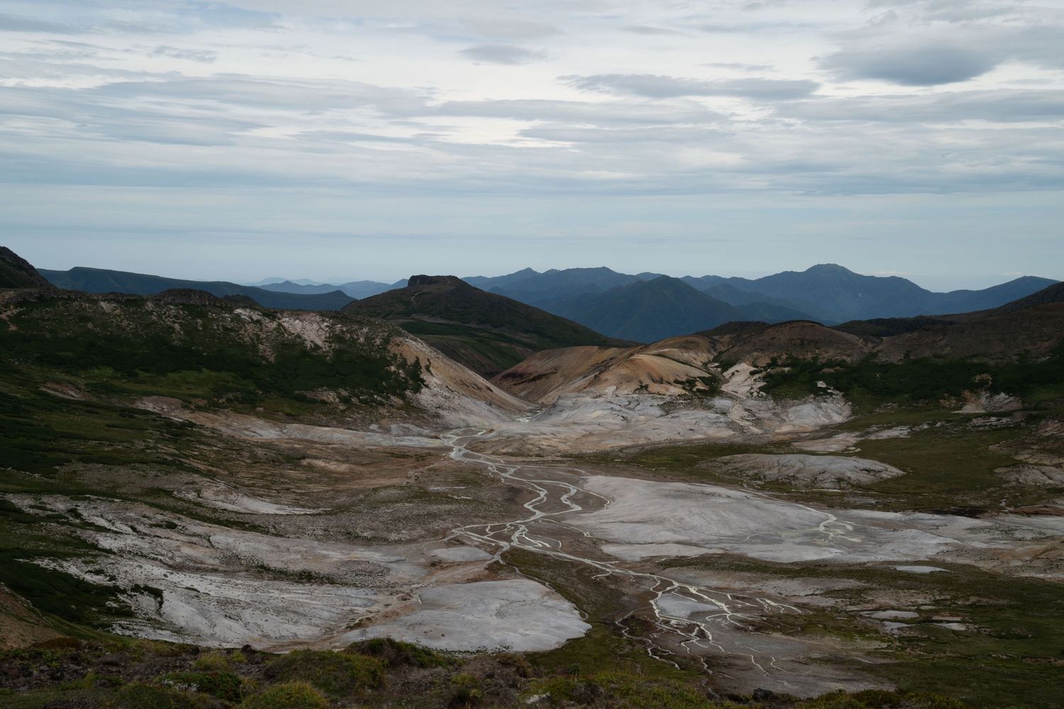 Aerial view of a stark mountain landscape with exposed geological features and distant ranges.