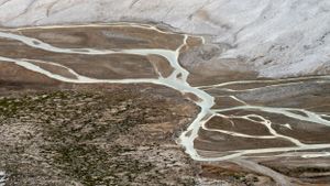 Snaking white paths wind through a barren mountain valley creating natural geometric patterns.