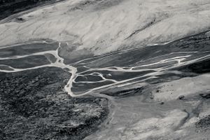 Aerial view of winding mountain trails through rugged volcanic terrain with white mineral deposits.
