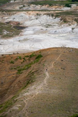 Hiking trail traverses across a barren hillside with white geothermal deposits in the background.