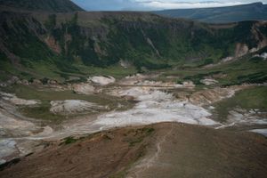Sweeping valley view of geothermal areas and mountains under cloudy skies.