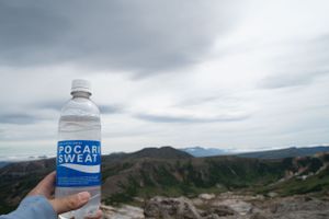 Water bottle held up against dramatic mountain landscape with cloudy sky.