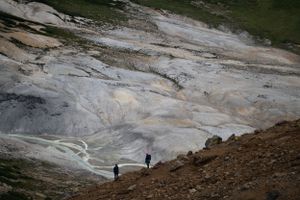 Hiking path crosses rocky volcanic terrain with distant mountain views.