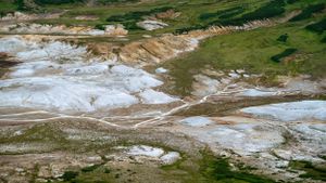 Aerial view of geothermal area showing white mineral deposits and green vegetation.