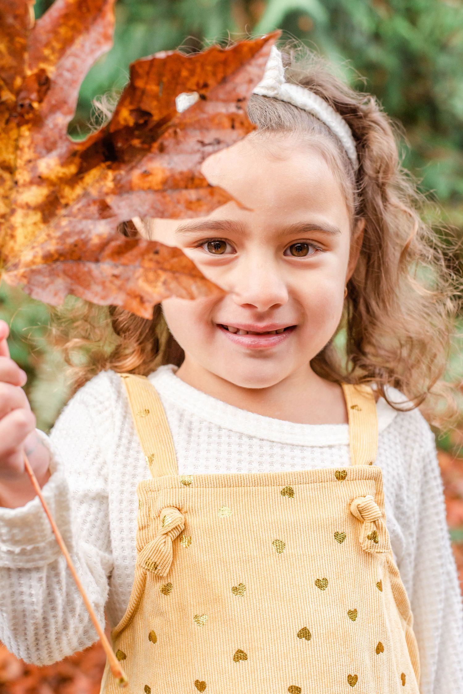 A playful autumn moment with a yellow dress and large orange leaf held up to the camera.