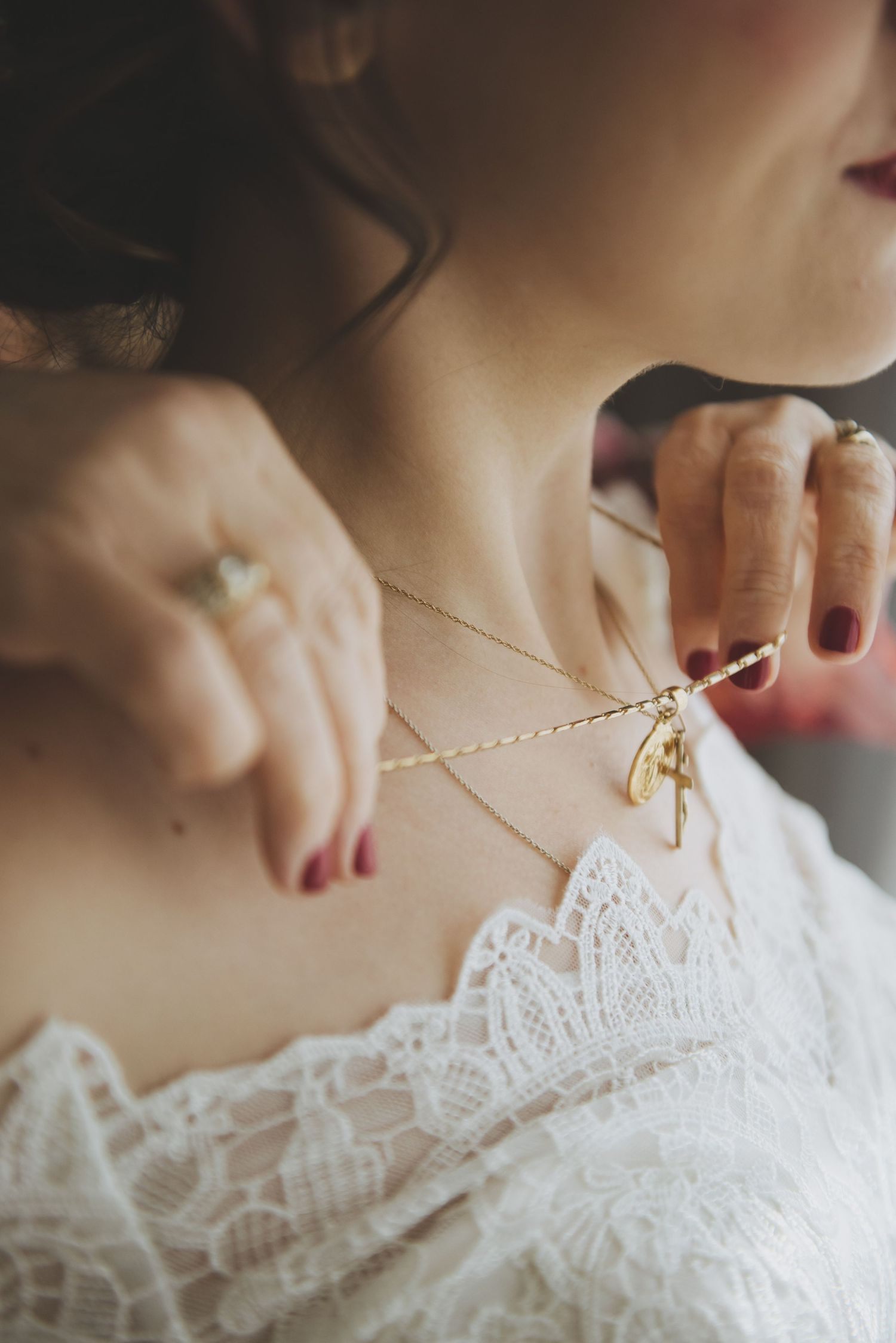 a mother places a  gold crucifix pendant and miraculous medal around her daughter who is dressed for her wedding day.