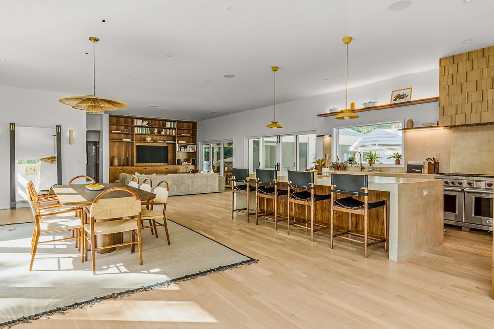 Modern open concept dining area with wooden tables, pendant lights, and large windows in a bright setting.