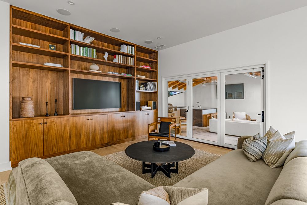 Modern living room with built-in wood shelving unit, TV, round coffee table and beige sectional sofa.