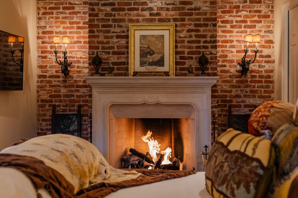 Cozy brick fireplace with roaring fire, white mantel, wall sconces, and framed art in elegant room.