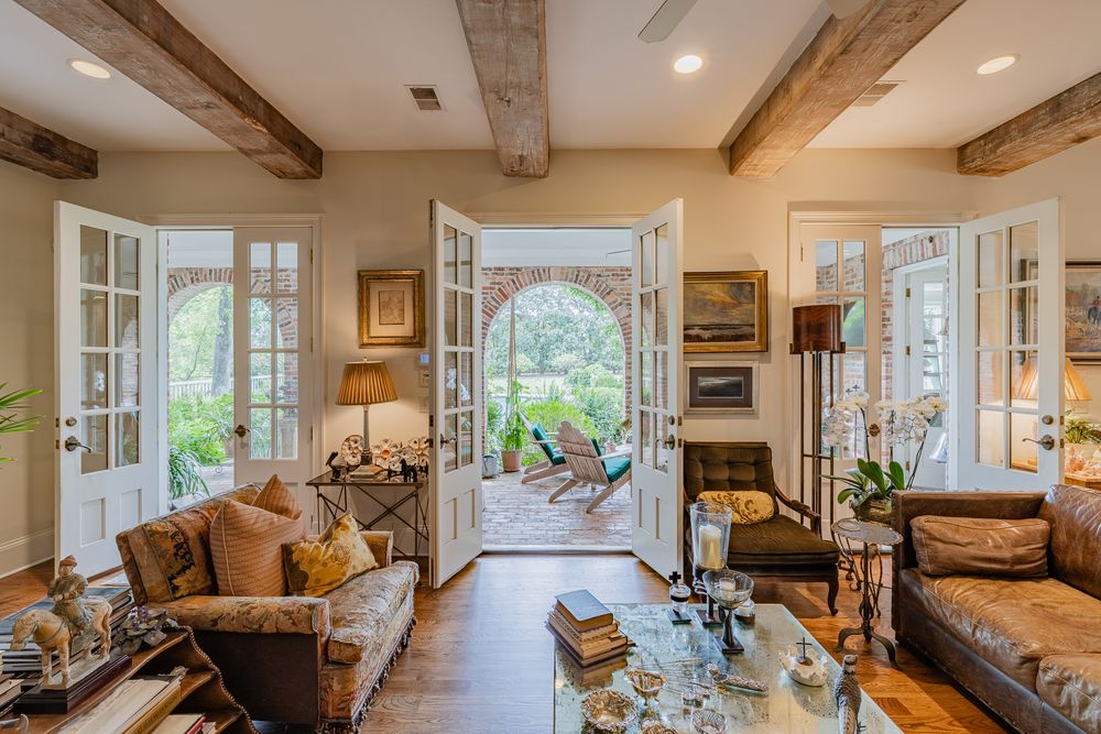 Elegant living room with rustic wood beam ceiling, French doors, arched entryway, and lush garden views.
