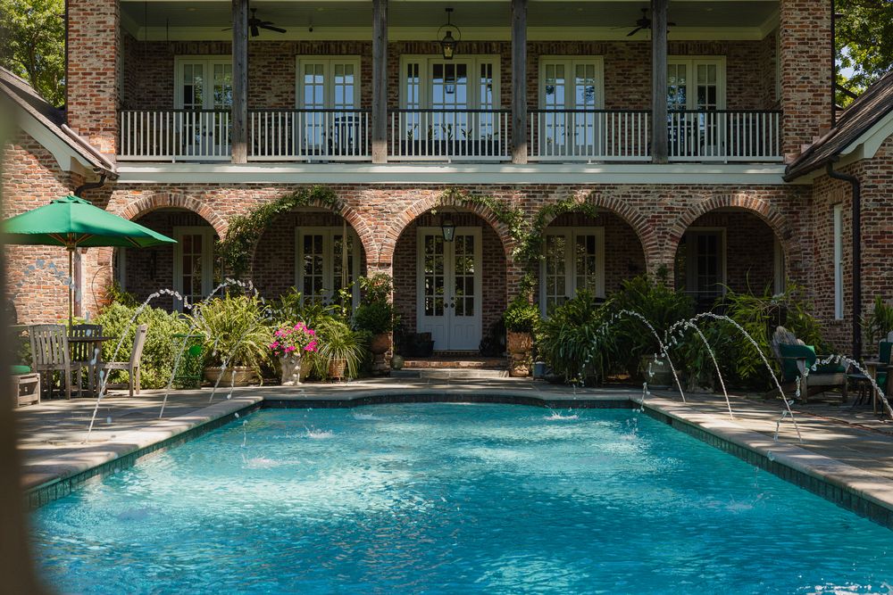 Luxurious outdoor pool with fountain jets surrounded by brick arches, balconies, and tropical landscaping.