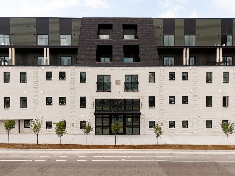 Modern multi-story apartment building with white brick facade, dark upper floors, and balconies lining a city street.