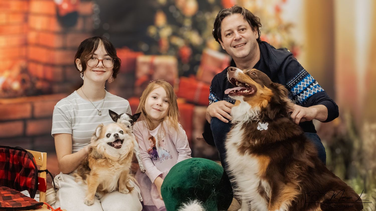 Family with pets poses for holiday portrait in front of decorated Christmas fireplace.
