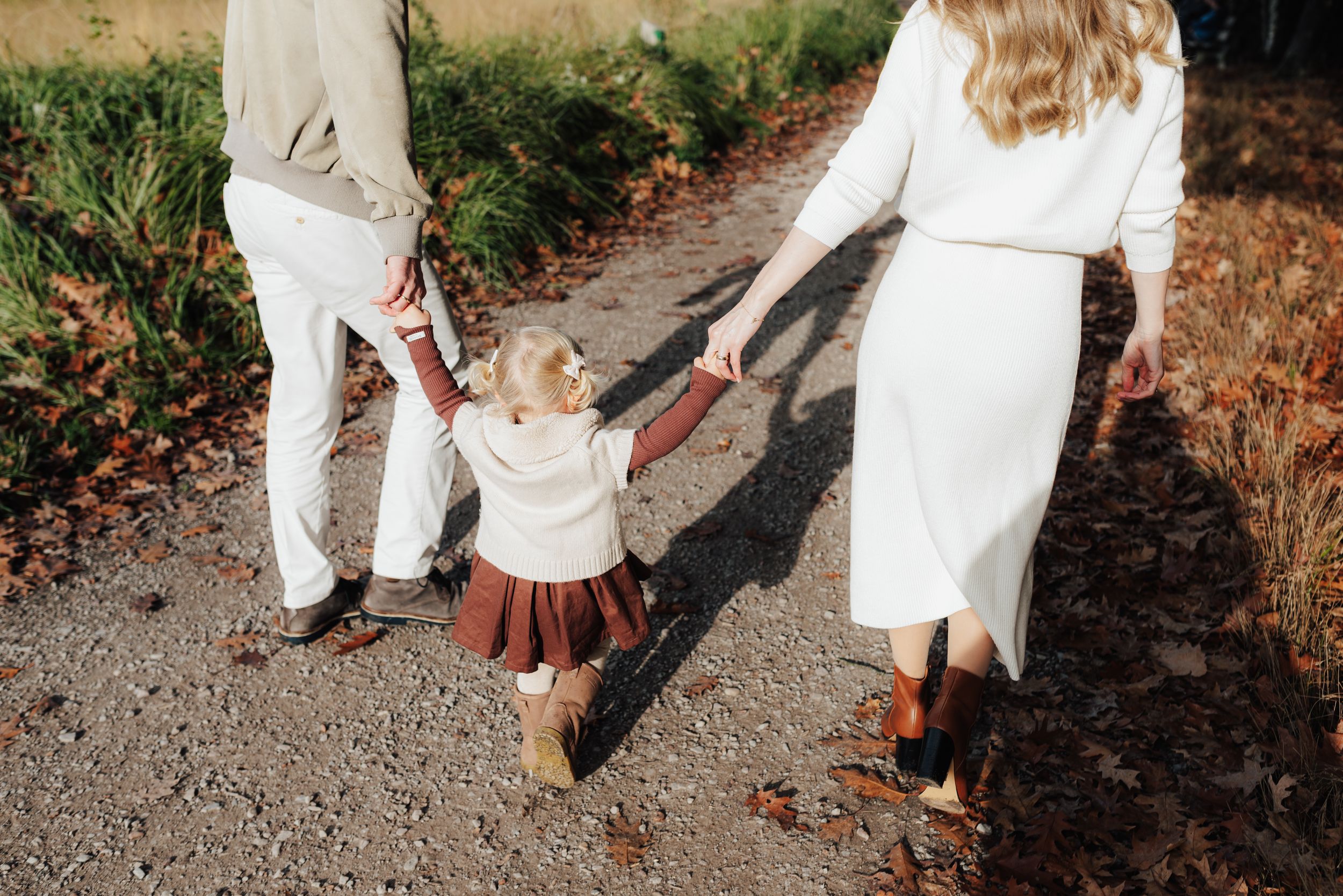People wearing coordinated neutral white and beige outfits walk in a line on a gravel path in a garden setting.