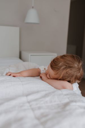 Small child sleeping peacefully on white bedding under soft lighting.
