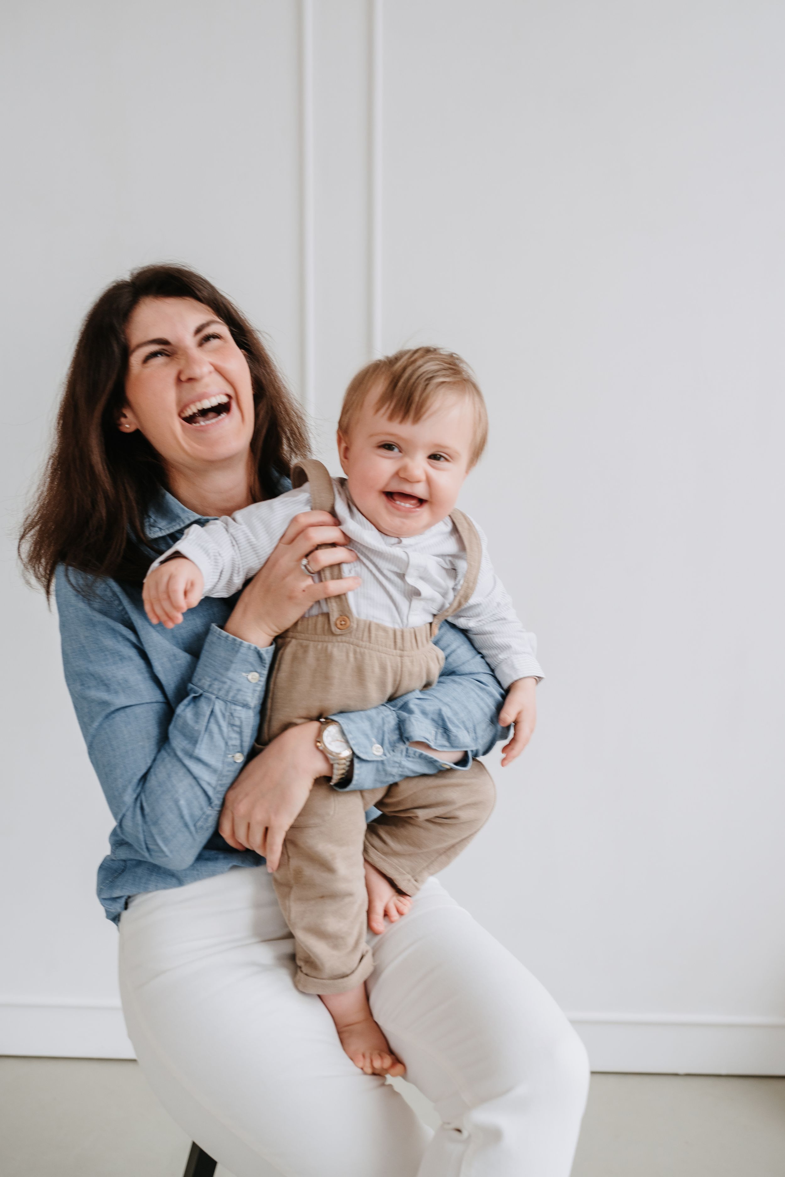 Joyful laughter shared between parent and baby against clean white wall background.