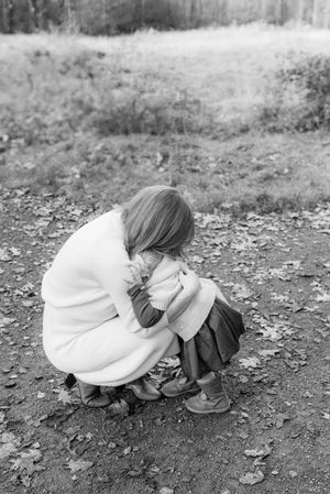A person in a white sweater crouches down on a dirt path in a black and white photograph.