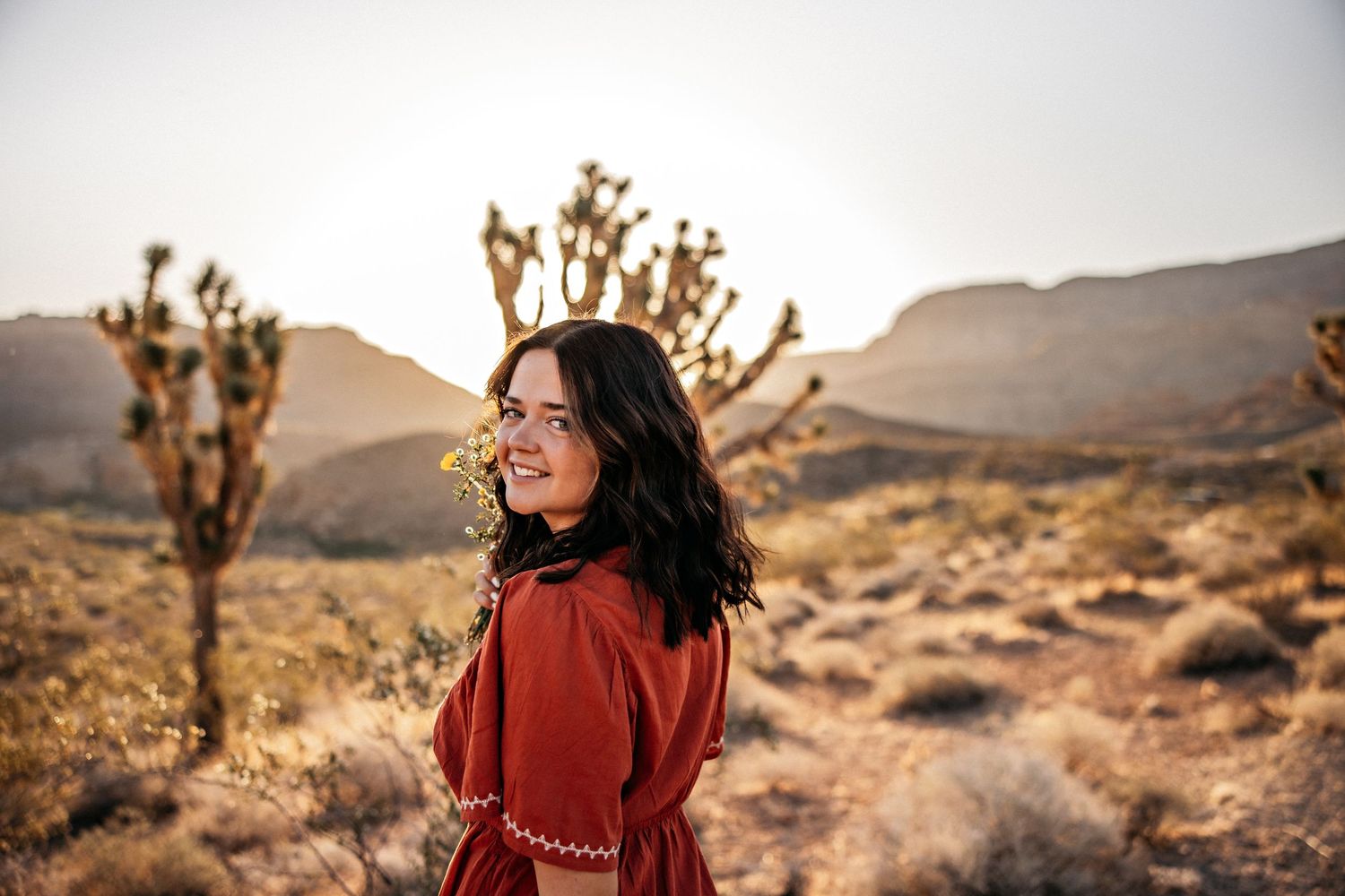 Woman with curly hair in blue top poses outdoors against desert backdrop.
