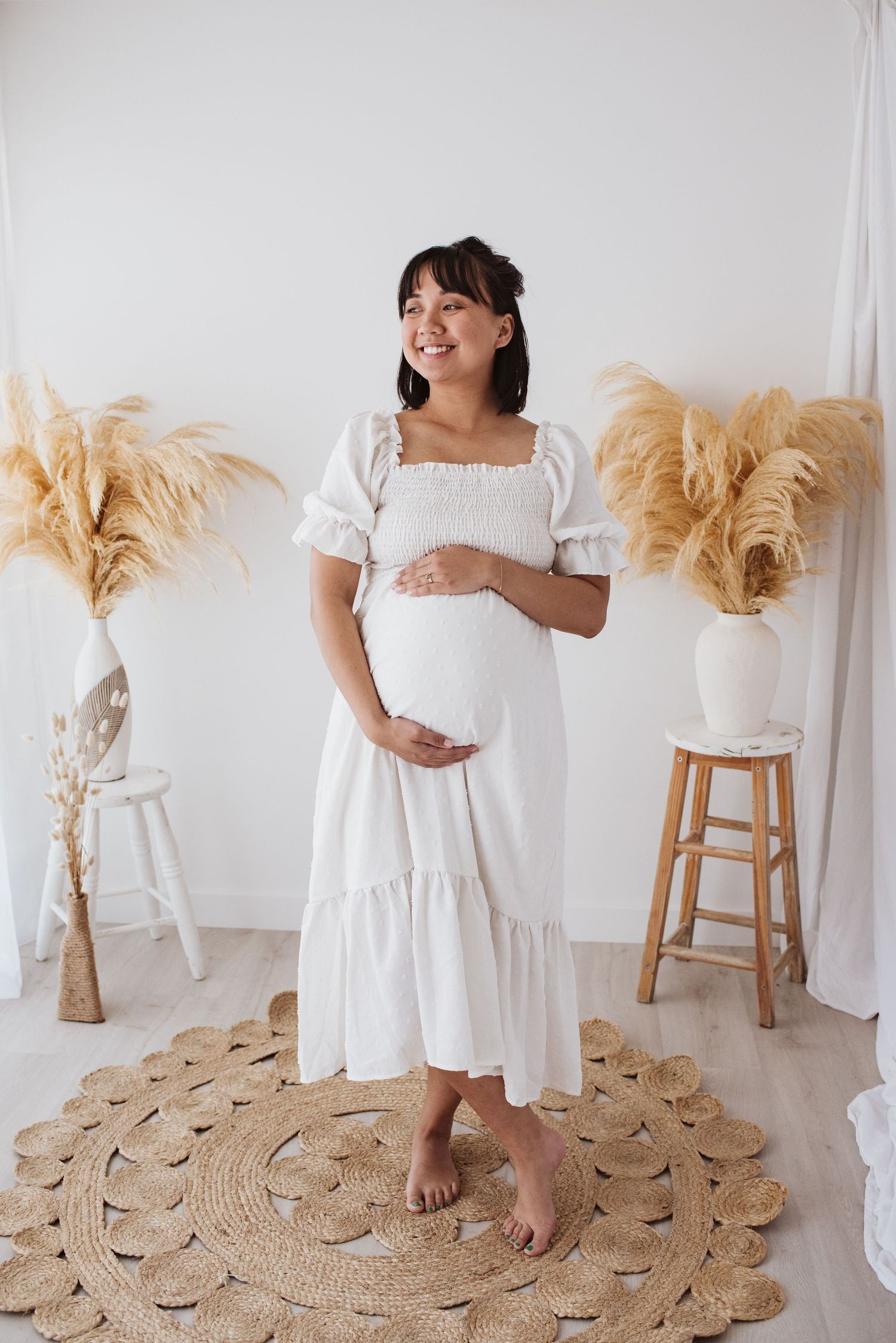 Indoor maternity portrait with white dress and boho pampas grass decor.
