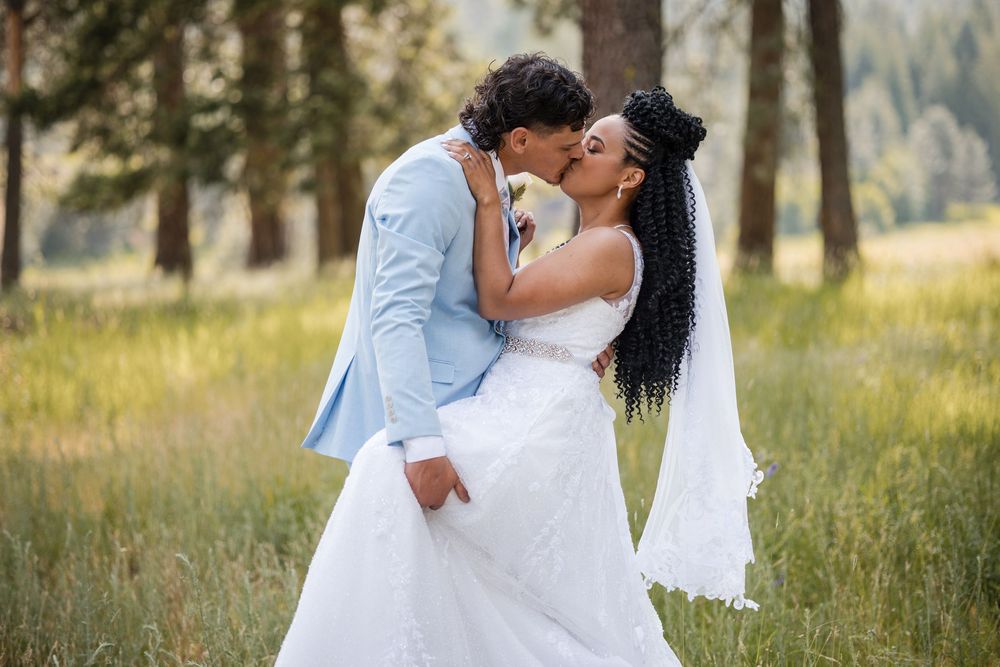 A wedding celebration moment outdoors in a sunlit meadow surrounded by towering trees in a natural forest setting.