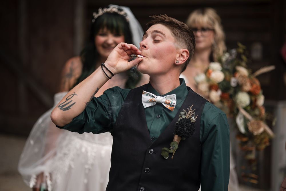 A well-dressed wedding guest in a bowtie and vest takes a celebratory drink at an indoor reception.