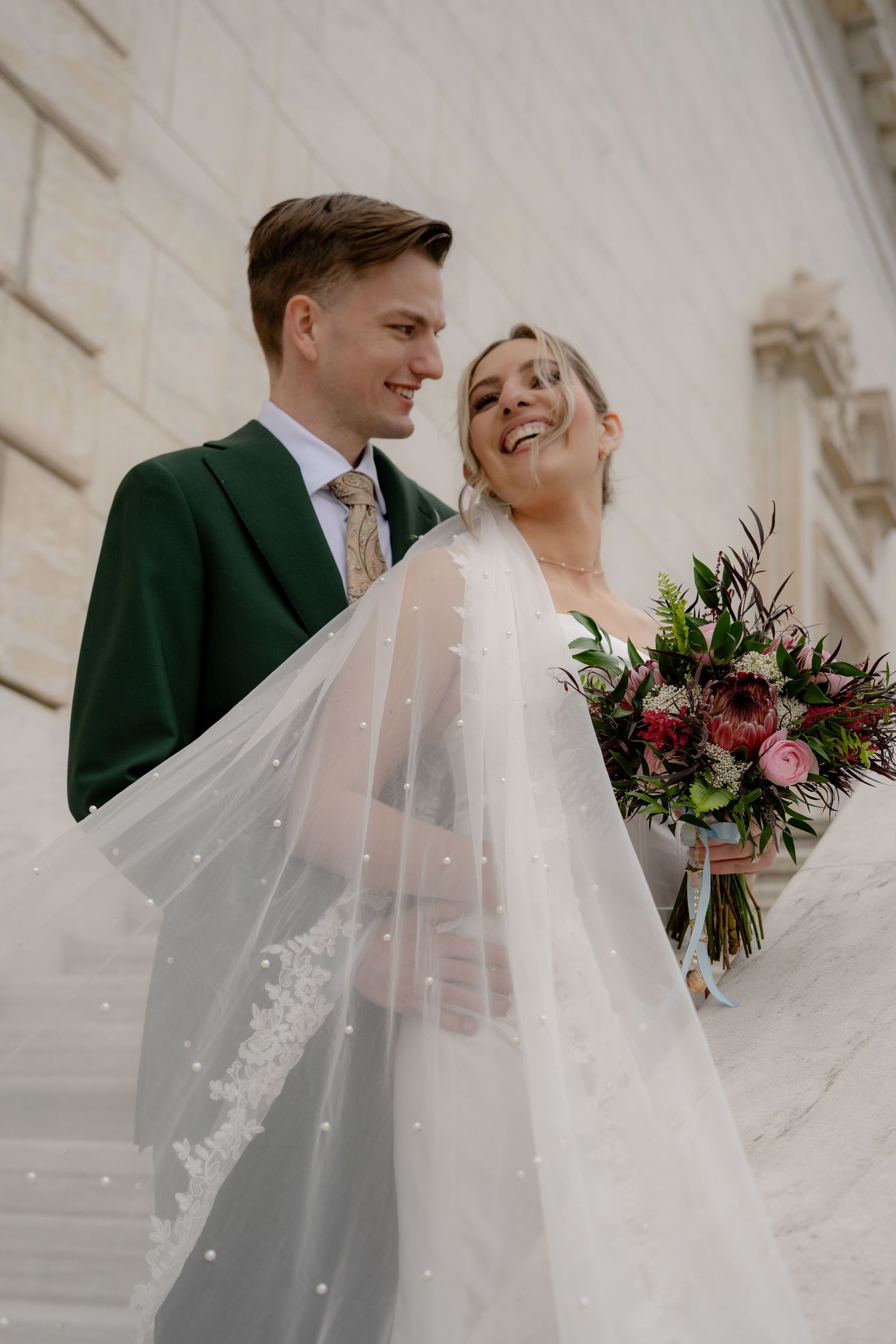 Elegant wedding couple shares joyful moment with burgundy bouquet.