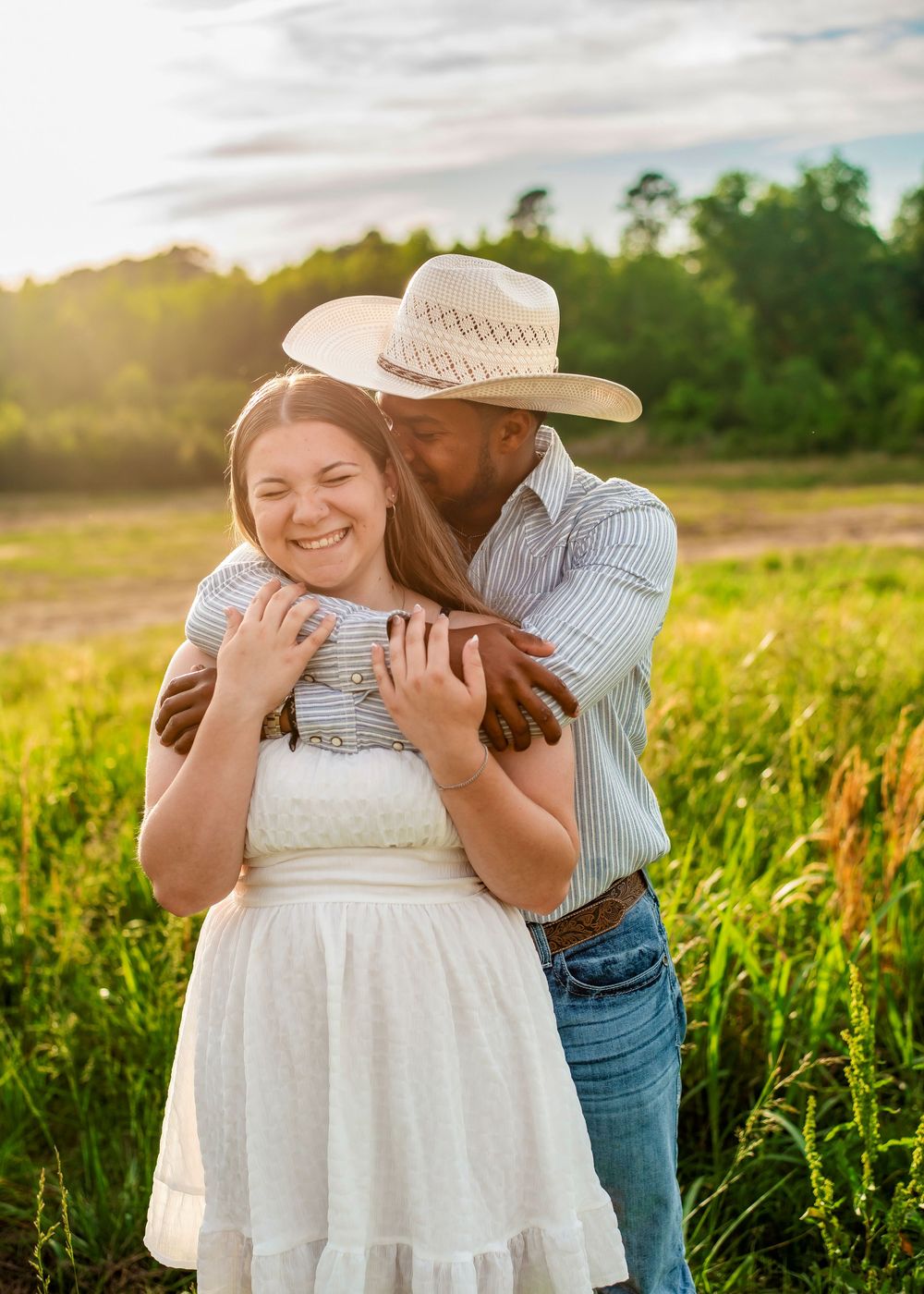 A romantic engagement photoshoot in a sunlit field shows a couple embracing during golden hour.