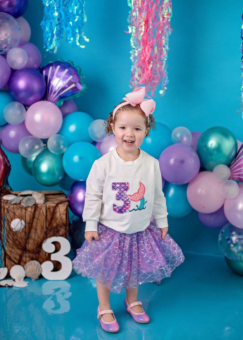 Purple and turquoise balloon decorations create a festive backdrop for a third birthday celebration photoshoot.