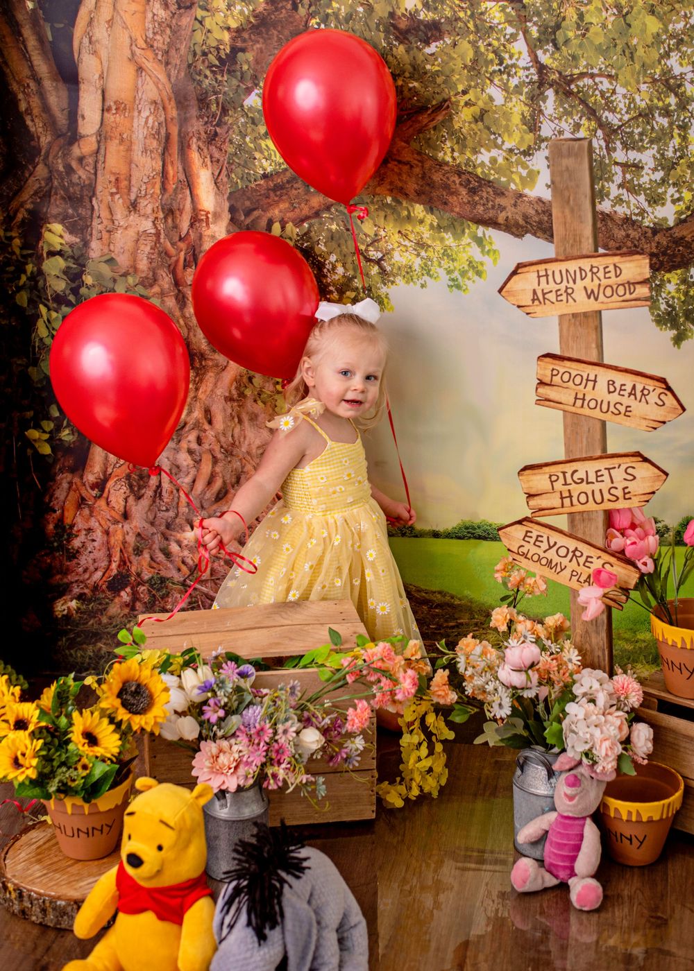 Whimsical woodland themed party setup with Winnie the Pooh decor, red balloons, sunflowers, and wooden directional signs.