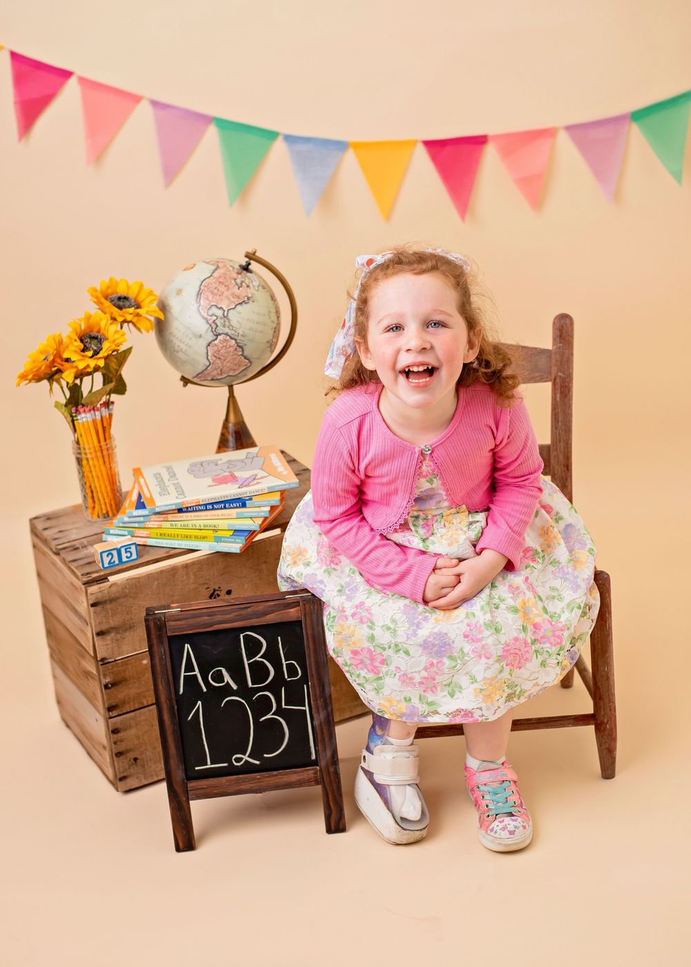 Colorful bunting hangs above a wooden crate display with educational props including a globe, chalkboard and sunflowers.