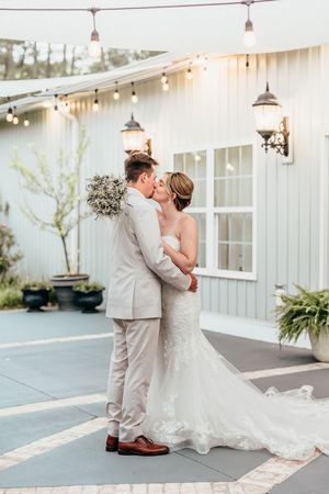 Couple celebrates wedding day with romantic dancing and embraces outside a white building with string lights.